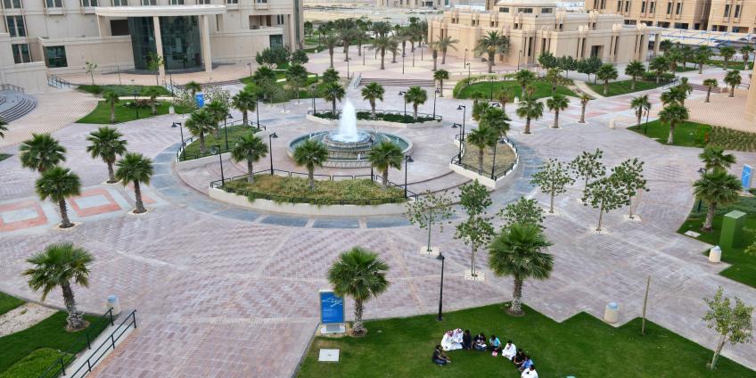 Trees and fountain on the eastern campus of Imam Abdulrahman bin Faisal University, students sitting on the grass in study circle.