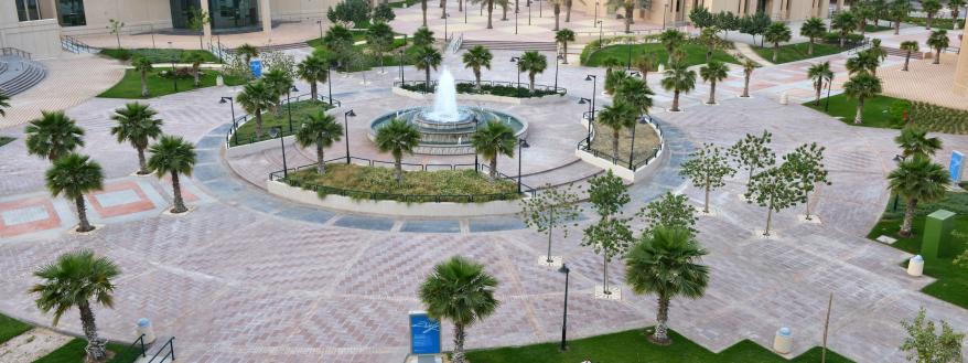 Trees and fountain on the eastern campus of Imam Abdulrahman bin Faisal University, students sitting on the grass in study circle.