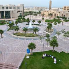 Trees and fountain on the eastern campus of Imam Abdulrahman bin Faisal University, students sitting on the grass in study circle.